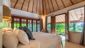 A spacious bedroom with a large bed, wooden ceiling, and a view of lush greenery through open doors. - Infinity Pool | Five Bedrooms | Beachfront Stay (Canggu)