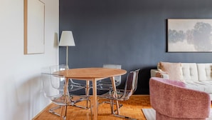 Un salon moderne avec un mur d’accent de couleur foncée, une table ronde en bois entourée de chaises, un canapé et une lampe.