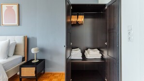 Une chambre moderne avec un lit, une table de chevet et une armoire contenant des vêtements suspendus et des serviettes pliées.