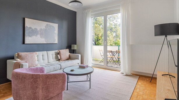Un salon moderne comprenant un canapé, un fauteuil et une table basse, une grande fenêtre donnant sur l’extérieur et un lampadaire.