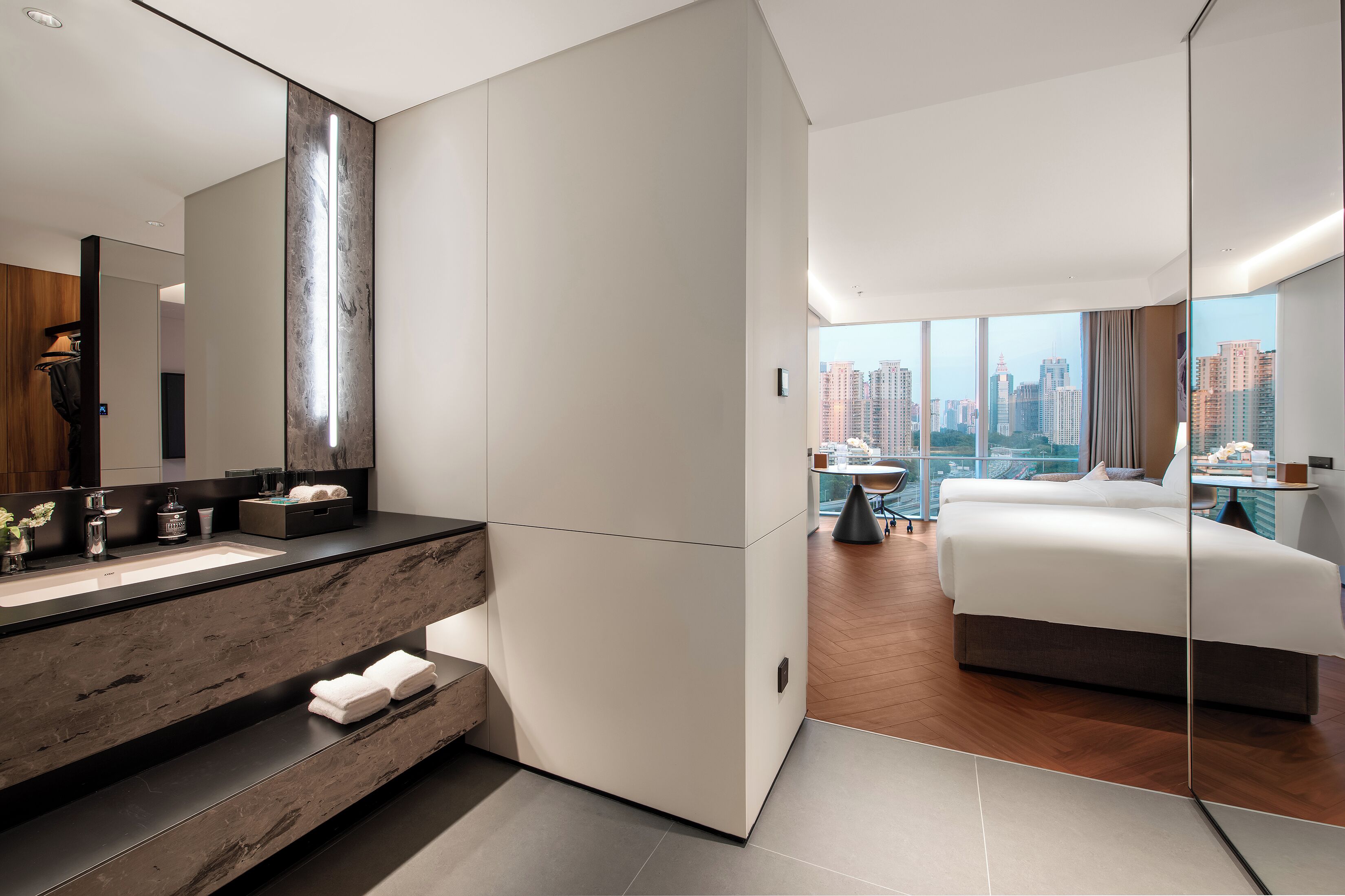 Ein modernes Hotelzimmer mit einem großen Bett, einem Badezimmer mit Marmorwaschtisch und Blick auf die Stadt.