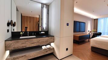 A modern hotel room with a large mirror, a wooden vanity, a flat-screen TV, a bed, and a seating area.
