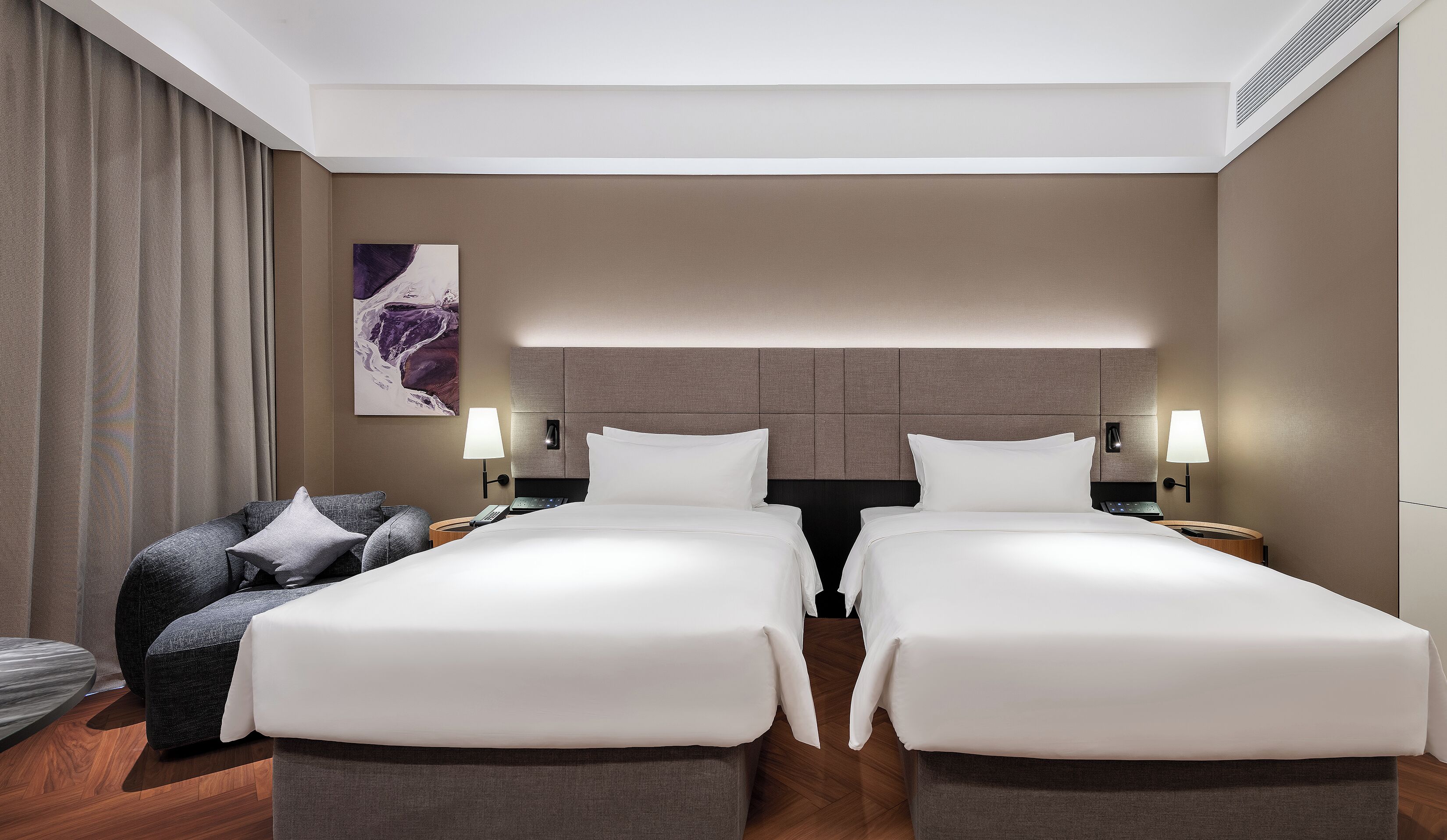 A hotel room with two beds, a sofa, a lamp, and a painting on the wall.