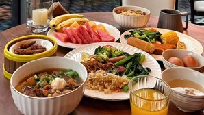 Una mesa de comedor con diferentes platos, un vaso de jugo de naranja y vistas de un paisaje urbano a través de grandes ventanales.