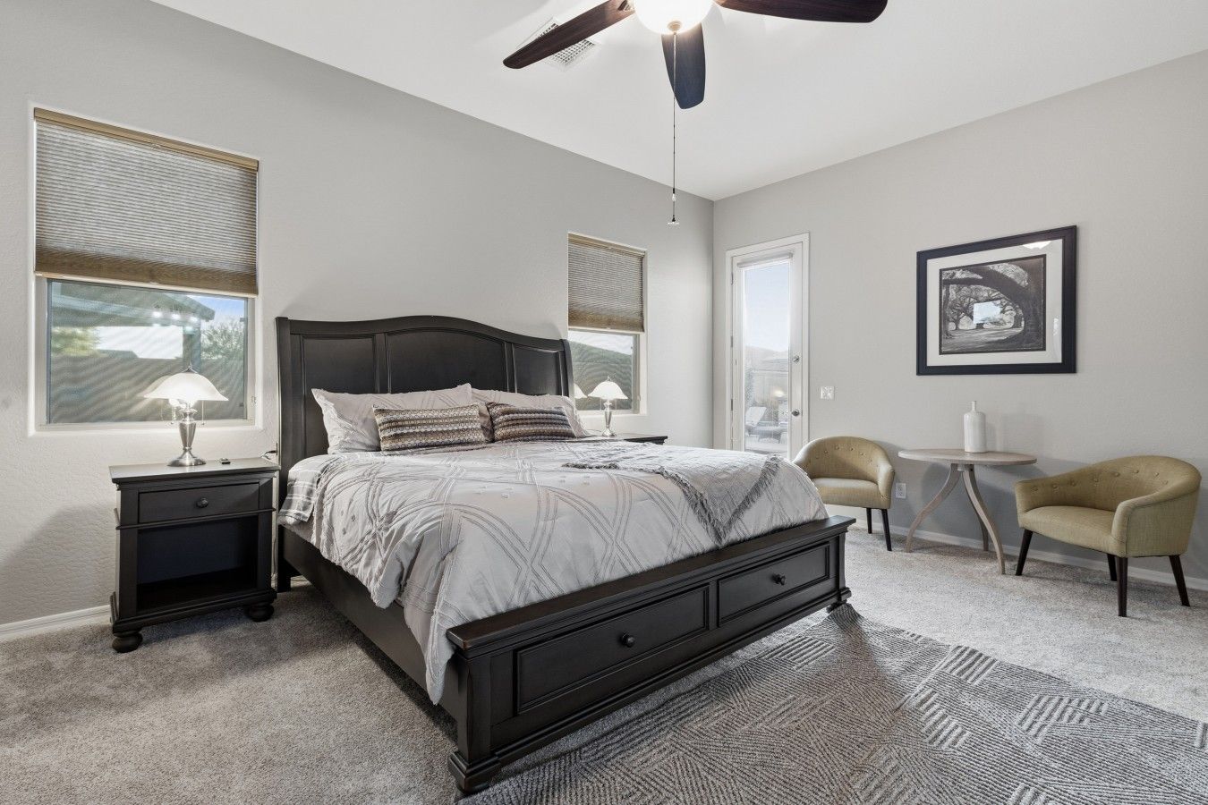 A bedroom with a dark wood bed, bedside lamps, a ceiling fan, and a view through a door.