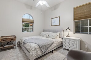 A bedroom with a bed, a nightstand, a desk, a chair, a ceiling fan, and two windows. - WoodHaven, Amazing Interior, Stunning Backyard, Combined Pool & Spa 11 x 20 Feet (Goodyear)