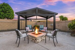 Une terrasse extérieure dotée d’un foyer, de sièges et d’une structure en forme de pergola.