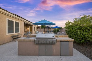 An outdoor kitchen area with a grill, seating, and umbrellas. - WoodHaven, Amazing Interior, Stunning Backyard, Combined Pool & Spa 11 x 20 Feet (Goodyear)