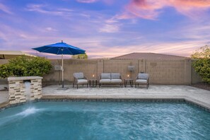 A backyard with a swimming pool, a stone wall, and a blue umbrella. - WoodHaven, Amazing Interior, Stunning Backyard, Combined Pool & Spa 11 x 20 Feet (Goodyear)
