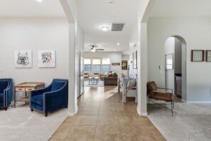 A spacious living room with a high ceiling, a dining area, and a kitchen visible through an archway. - WoodHaven, Amazing Interior, Stunning Backyard, Combined Pool & Spa 11 x 20 Feet (Goodyear)