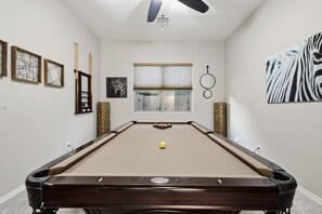 A pool table in a room with a ceiling fan, framed artwork, and a window with blinds. - WoodHaven, Amazing Interior, Stunning Backyard, Combined Pool & Spa 11 x 20 Feet (Goodyear)