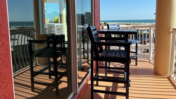 A balcony with a table and chairs, a glass door, and a view of the ocean and buildings. - Vitamin SEA Condo 7️⃣2️⃣7️⃣2️⃣5️⃣1️⃣8️⃣6️⃣5️⃣9️⃣ (Treasure Island)
