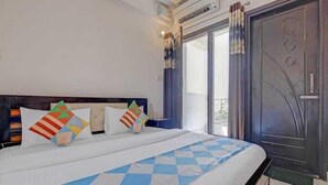 Quarto de hotel com uma cama grande, uma porta de madeira escura e uma janela com cortinas.