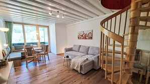 Un amplio salón con una escalera de madera, un sofá gris, suelo de madera y un comedor con sillas y una mesa.