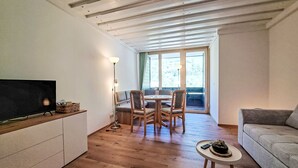 Una sala de estar moderna con piso de madera, televisor de pantalla plana, zona de comedor con mesa y sillas, y un sofá.