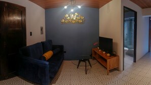 Un salon avec un canapé bleu foncé, une table basse en bois, un téléviseur et un élément décoratif mural.