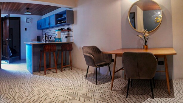 Une cuisine moderne avec des meubles bleus, une table à manger en bois avec deux chaises et un grand miroir au mur.