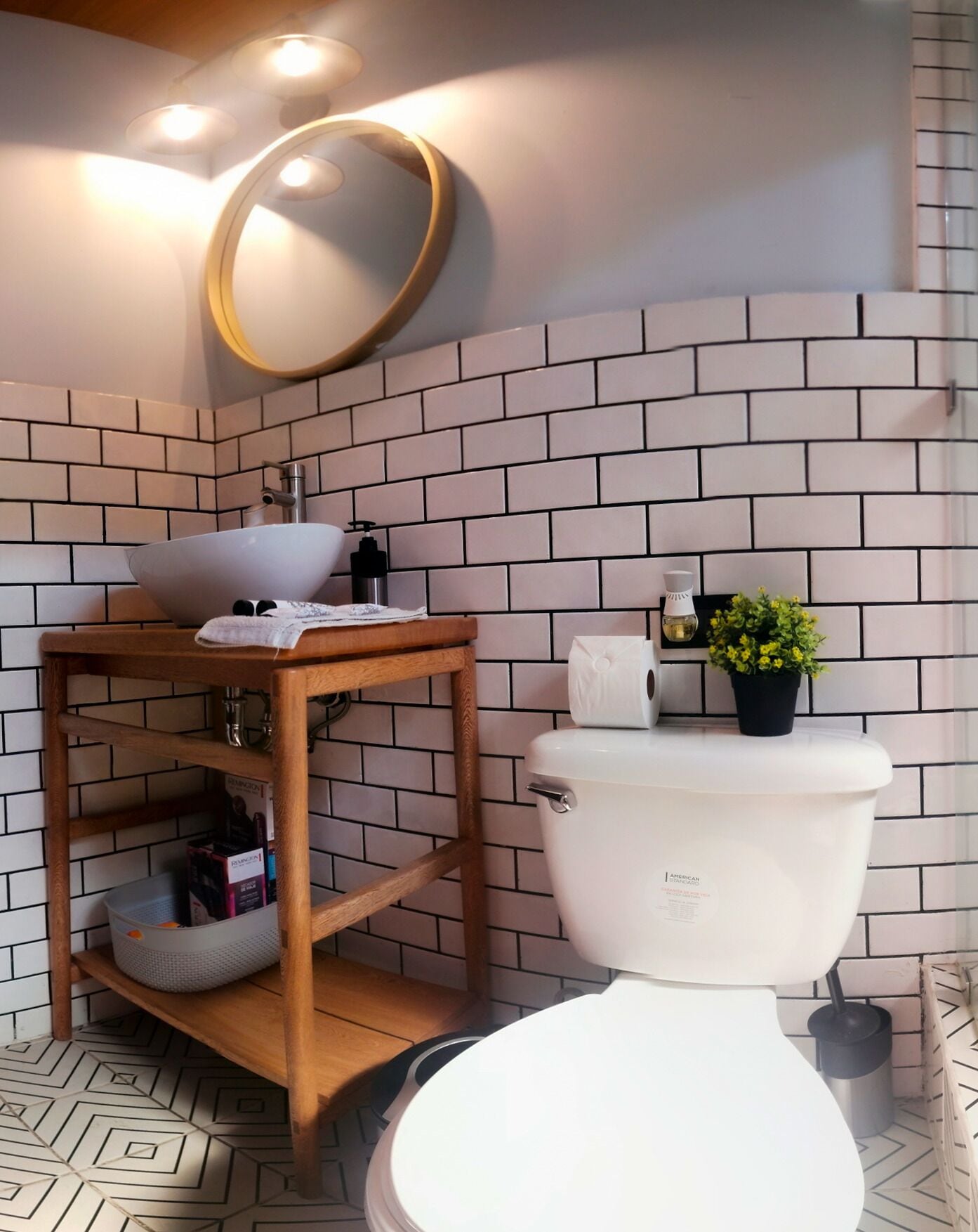 Un bagno con il water bianco, uno scaffale di legno con articoli da toilette, una piccola pianta in vaso e uno specchio a parete.
