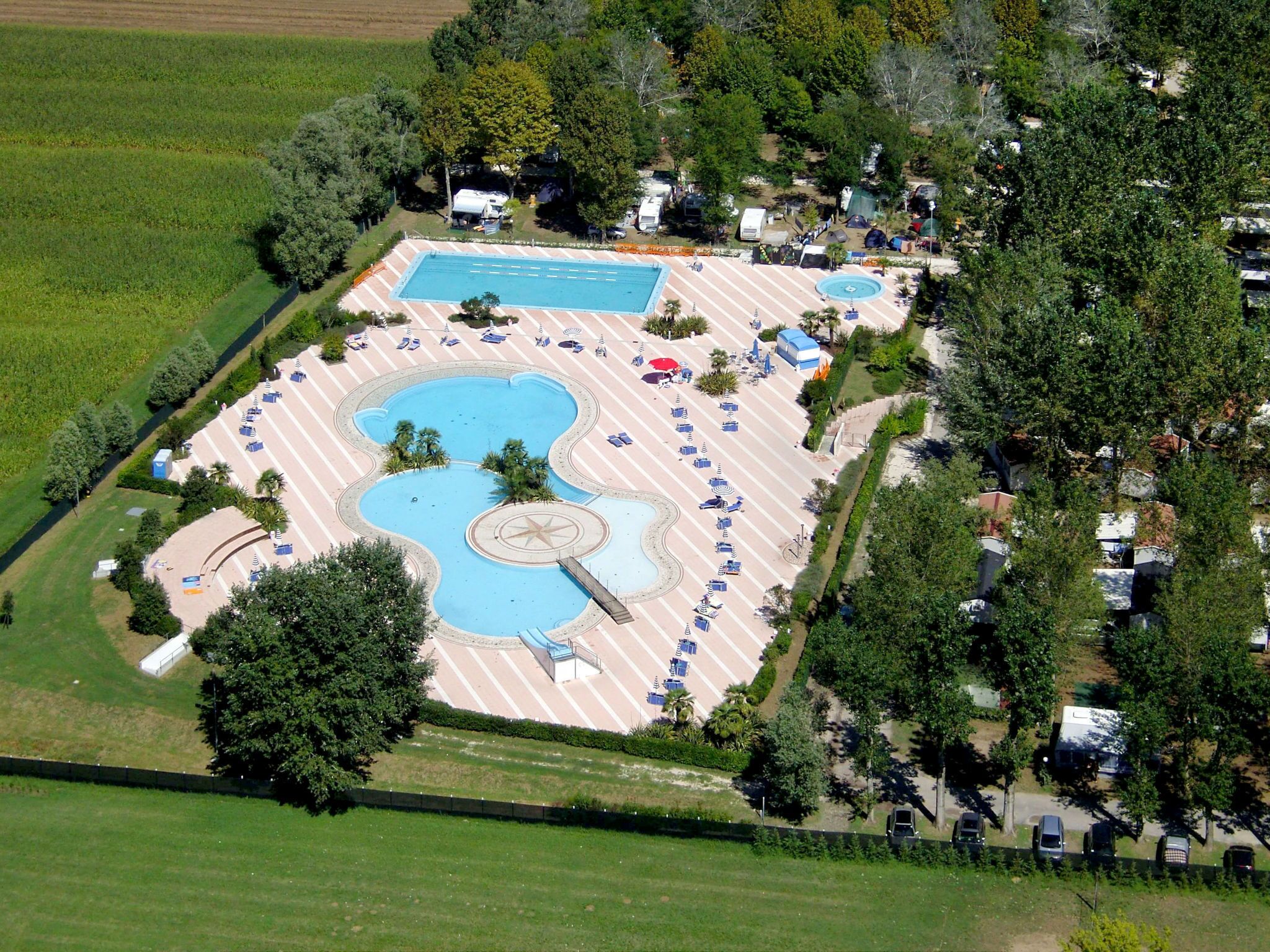 An aerial view of a resort with a large central pool, multiple smaller pools, and a variety of sun loungers and umbrellas.