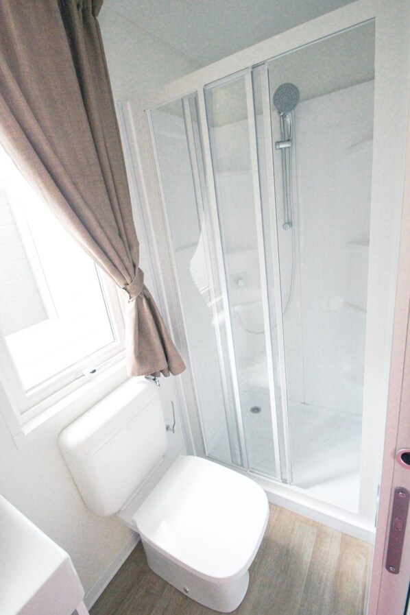 A bathroom with a toilet, a shower enclosure, and a window with curtains.
