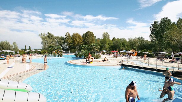 A swimming pool area with tiled flooring, lounge chairs, and umbrellas.