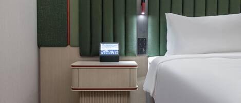 A modern hotel room with a bed, a nightstand with a digital clock, and a green headboard.
