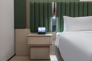 A modern hotel room with a bed, a nightstand with a digital clock, and a green headboard.