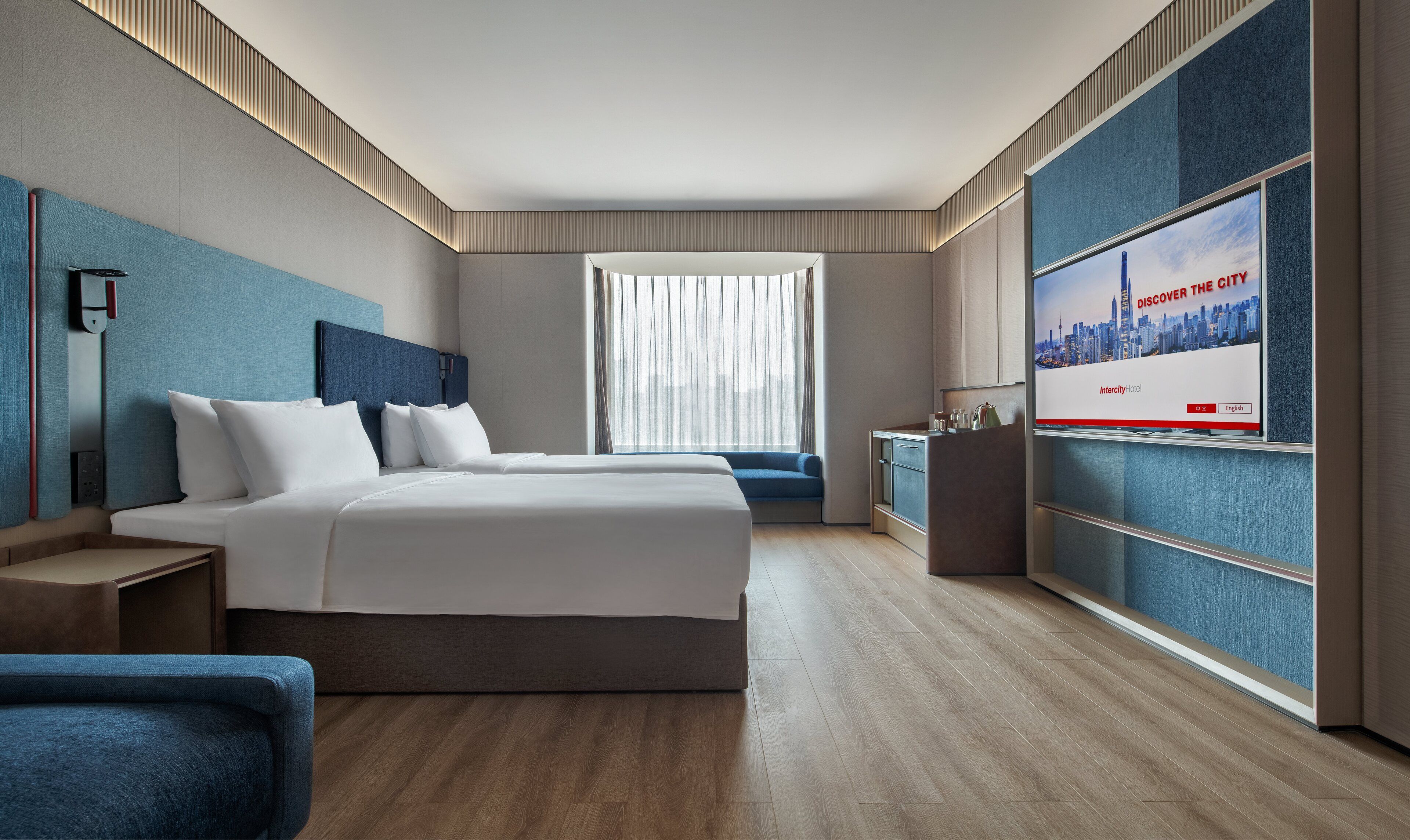 Een moderne hotelkamer met een groot bed, een zithoek, een televisie en uitzicht over de stad.