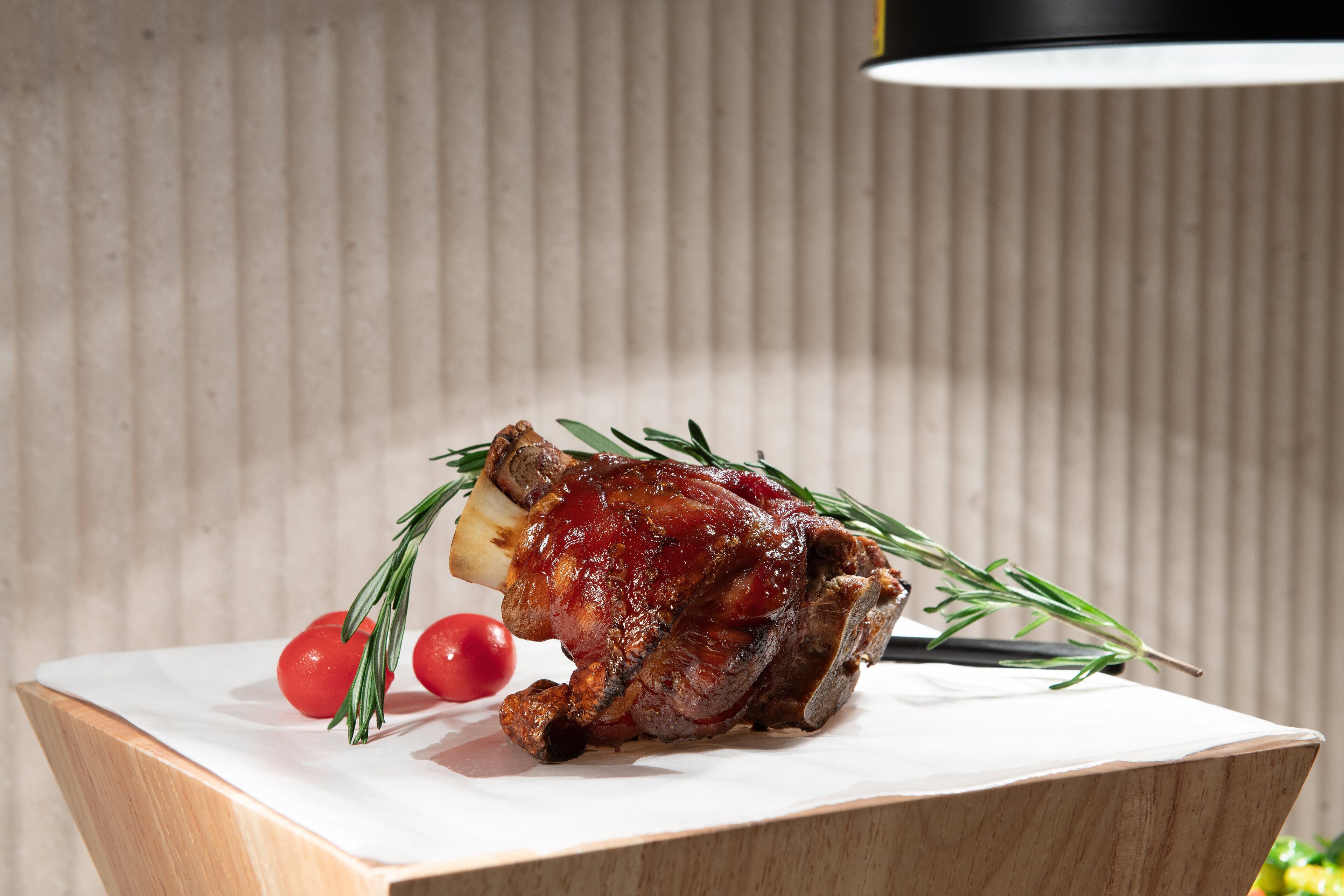 Un jambon rôti, garni de romarin et de tomates cerises, présenté sur une planche en bois.