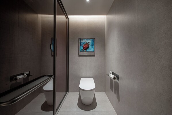 A modern bathroom with a toilet, a glass shower enclosure, and a framed artwork on the wall.