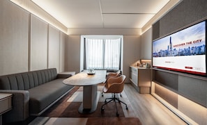 Une chambre d’hôtel moderne dotée d’un grand téléviseur diffusant une vue sur la ville, d’un canapé, d’une table à manger et d’un petit espace bureau.