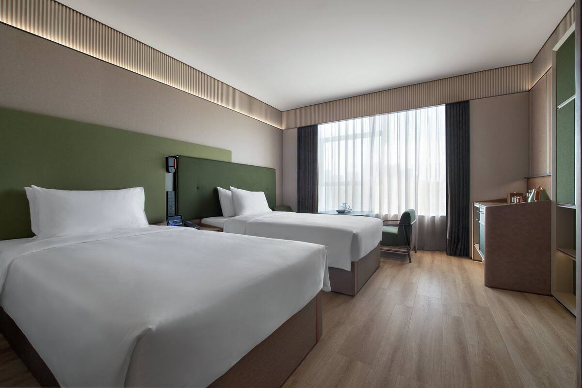 Ein Hotelzimmer mit zwei Betten, einem Schreibtisch, einem Stuhl und einem Fenster mit Vorhängen.