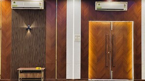 A modern hotel lobby with wooden paneling, two air conditioning units, a small table with a yellow object, and a ceiling light fixture. - Anand Resort (Durg)