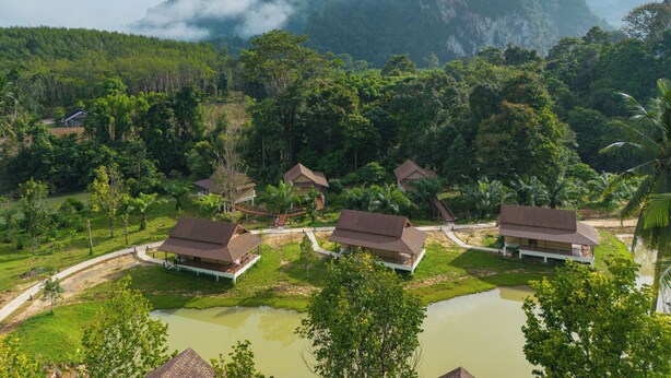 Een resort met meerdere bungalowgebouwen, omgeven door weelderige begroeiing en een groot wateroppervlak.