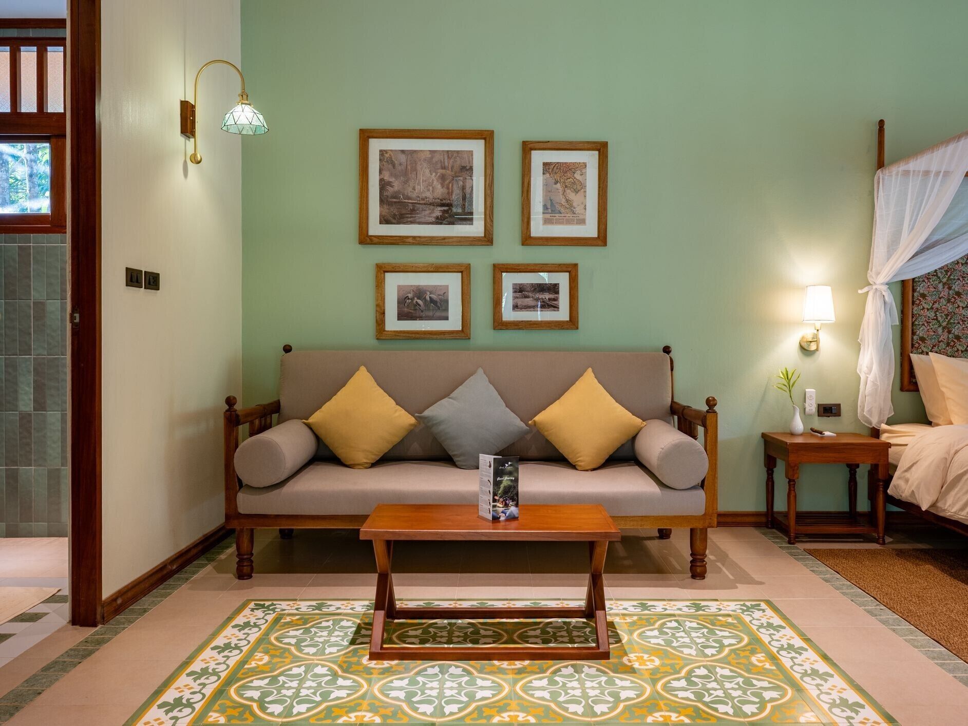 Une pièce comprenant un canapé, une table basse et un lit à baldaquin. Des tableaux encadrés ornent le mur, et une lampe est posée sur la table d’appoint.