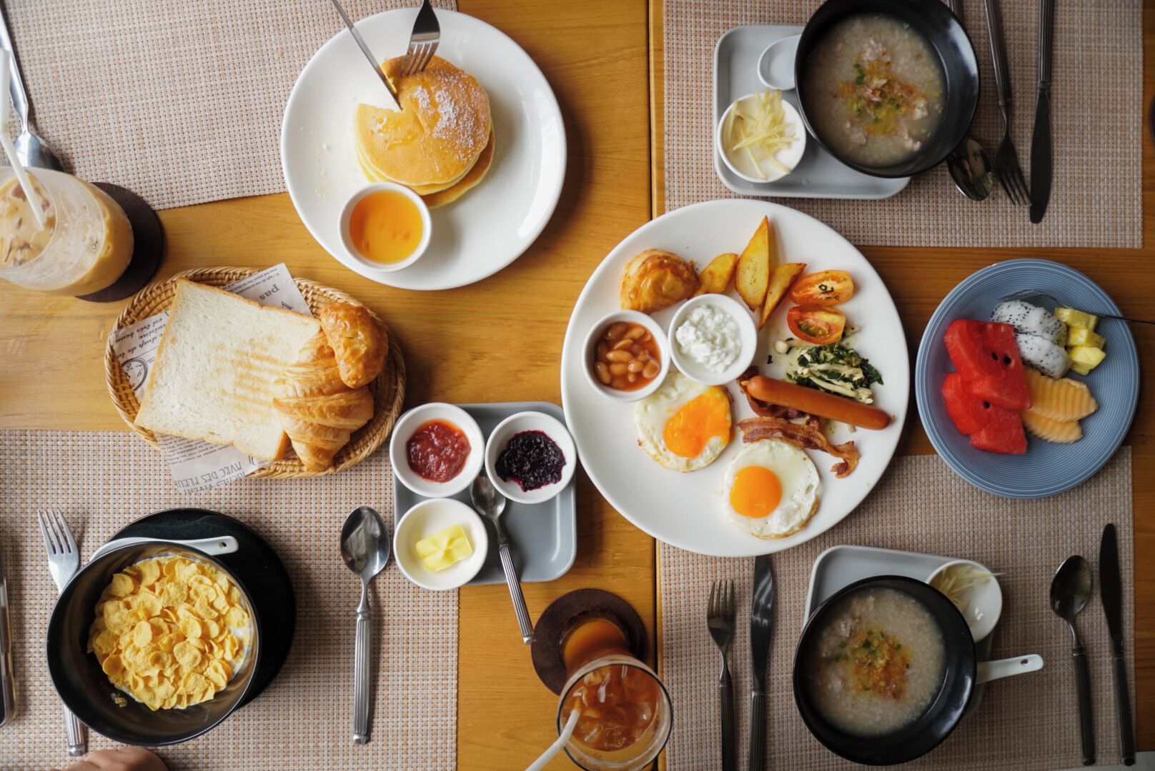 Ein reichhaltiges Frühstücksbuffet mit Pfannkuchen, Eiern, Speck, Toast und verschiedenen Beilagen auf einem Holztisch.