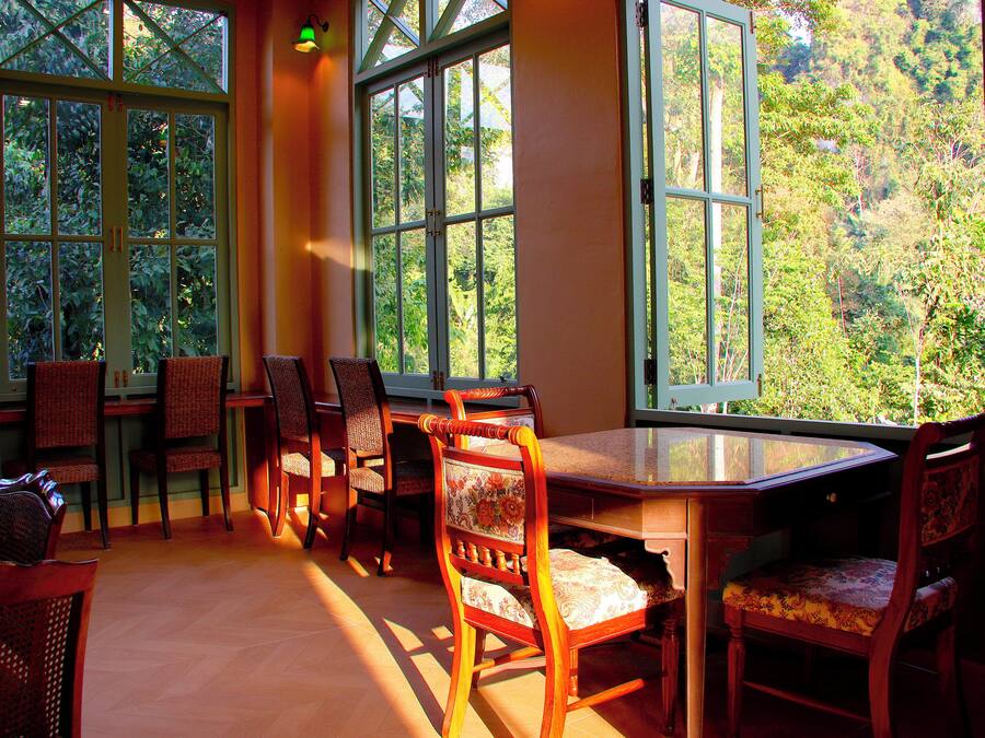 Un espace repas avec une table et des chaises en verre, de grandes fenêtres donnant sur un paysage verdoyant et un éclairage intérieur chaleureux.