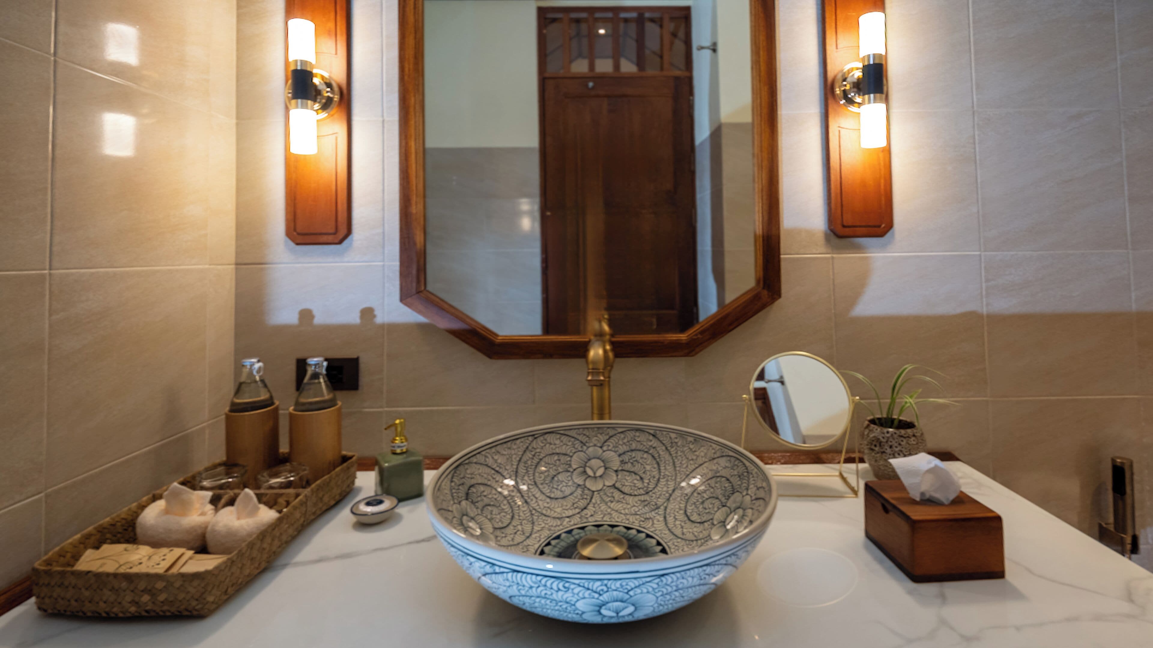 Un baño con un lavamanos grande y decorativo, una puerta de madera y dos luces fijadas a la pared.