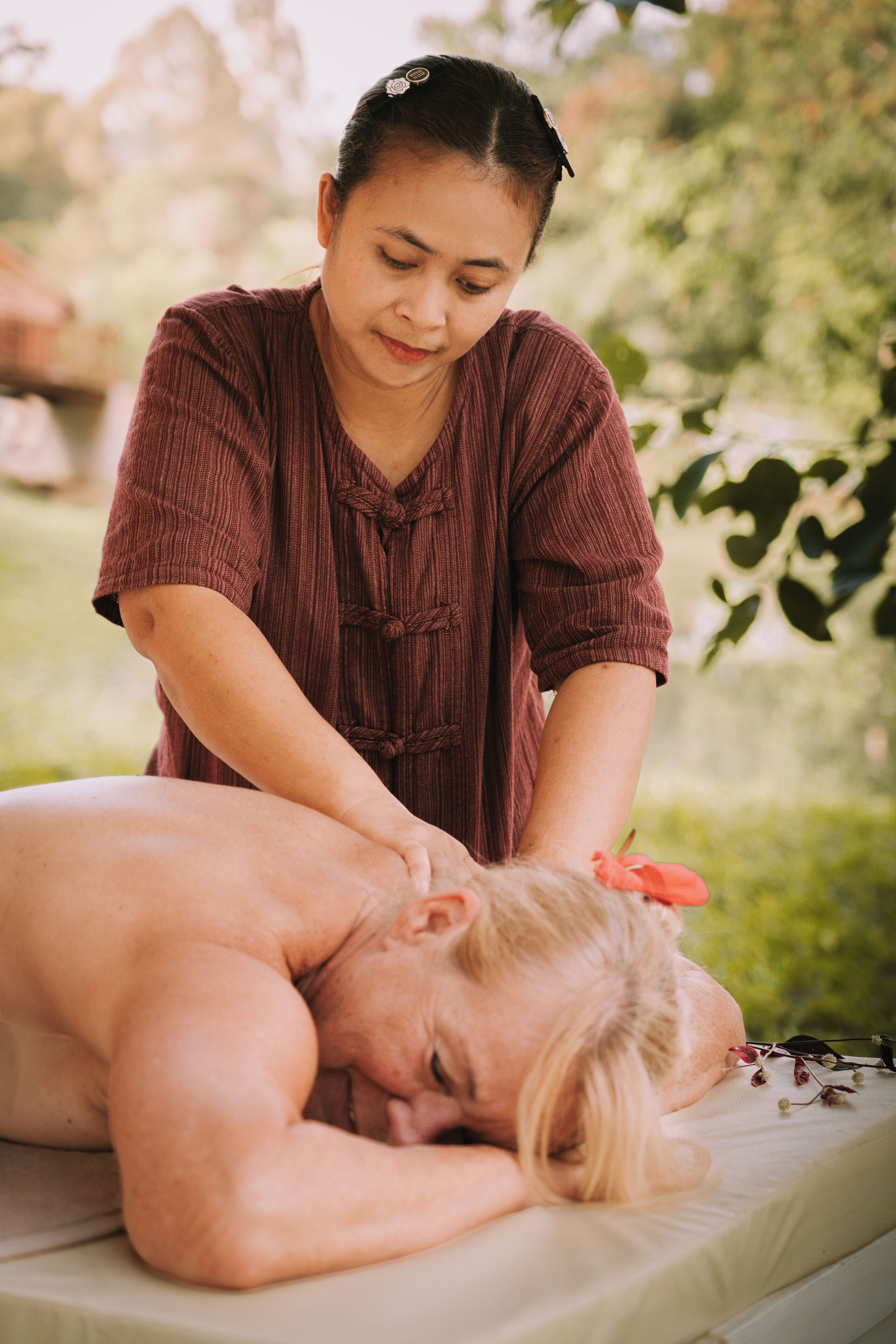 A massage therapy session in an outdoor setting with greenery in the background.
