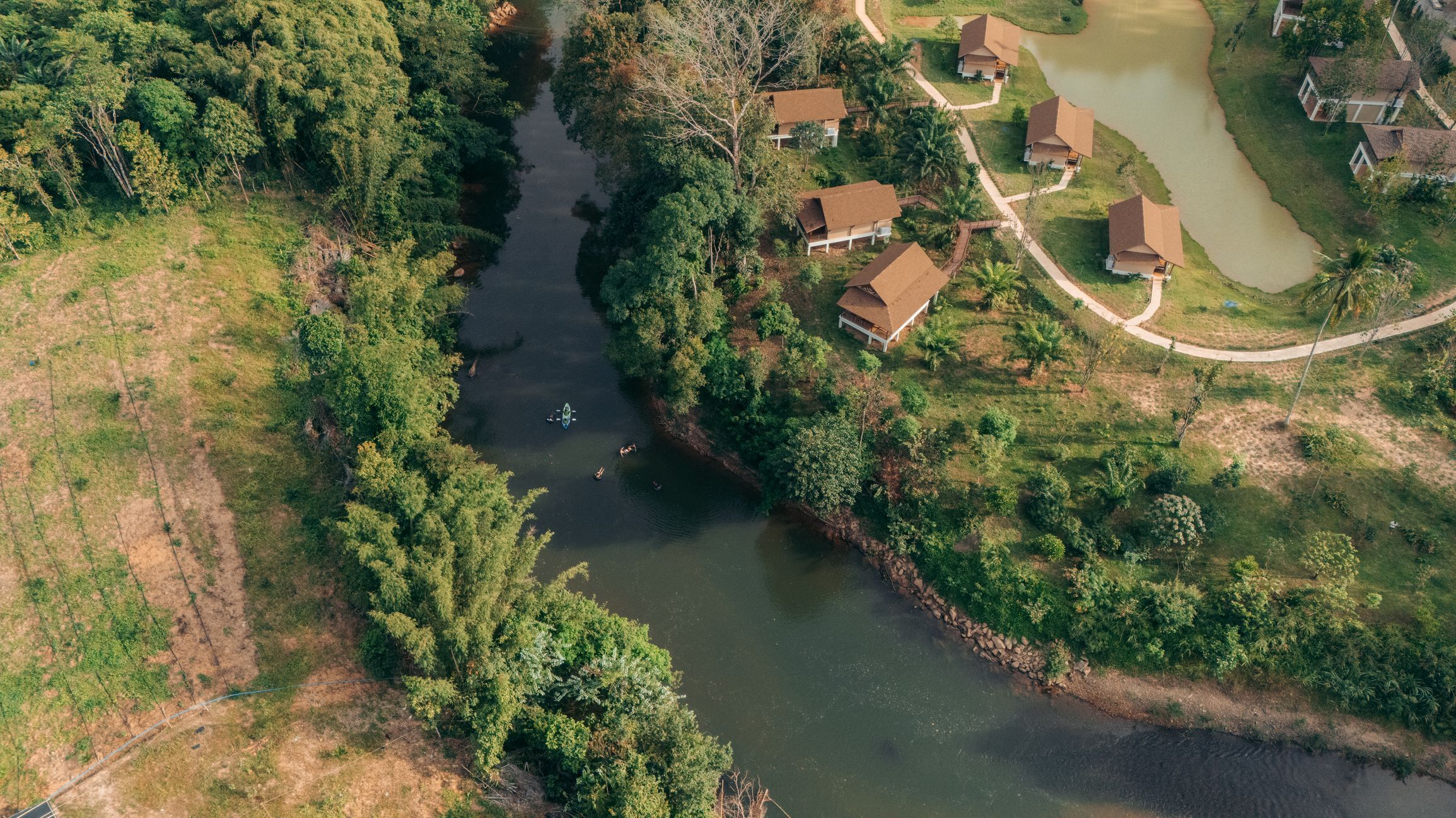 Vista aérea de um rio serpenteando por uma área residencial, com casas em ambas as margens.