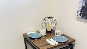 A small dining area with a wooden table and matching benches, a candle, and a mug with a rainbow design.