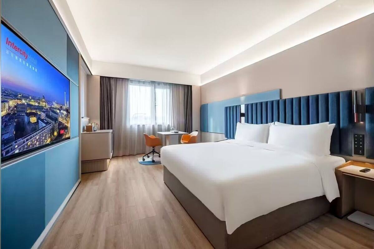 Une chambre d’hôtel avec un grand lit, un bureau avec une chaise, un téléviseur fixé au mur et une fenêtre avec des rideaux.