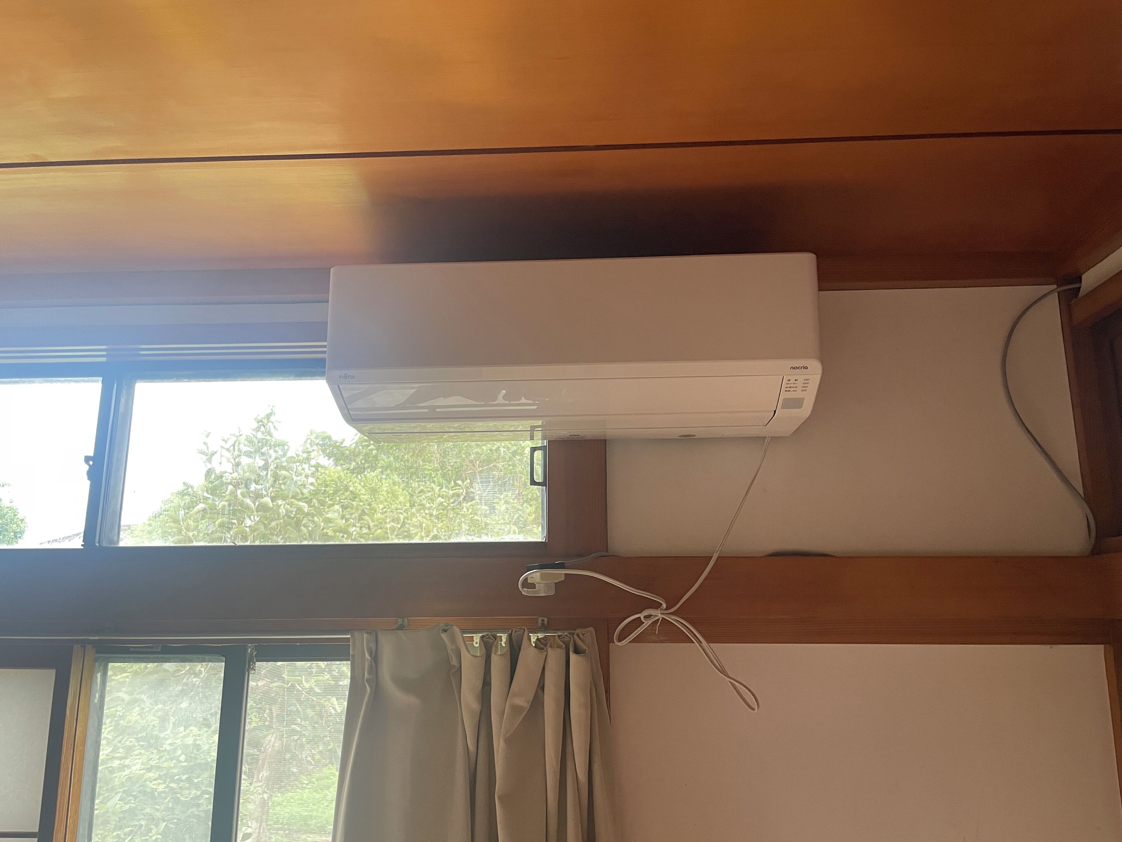A room with a window, a curtain, and an air conditioning unit mounted on the wall.