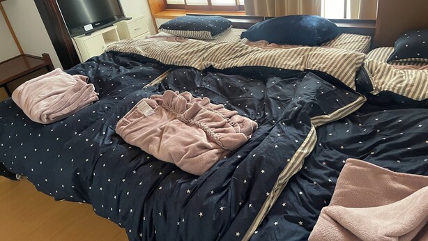 Quarto com cama, almofadas, manta, televisão e janela.