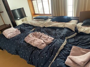 A bedroom with a bed, pillows, a blanket, a TV, and a window. - Tensen Inn on the bay (Nikaho)