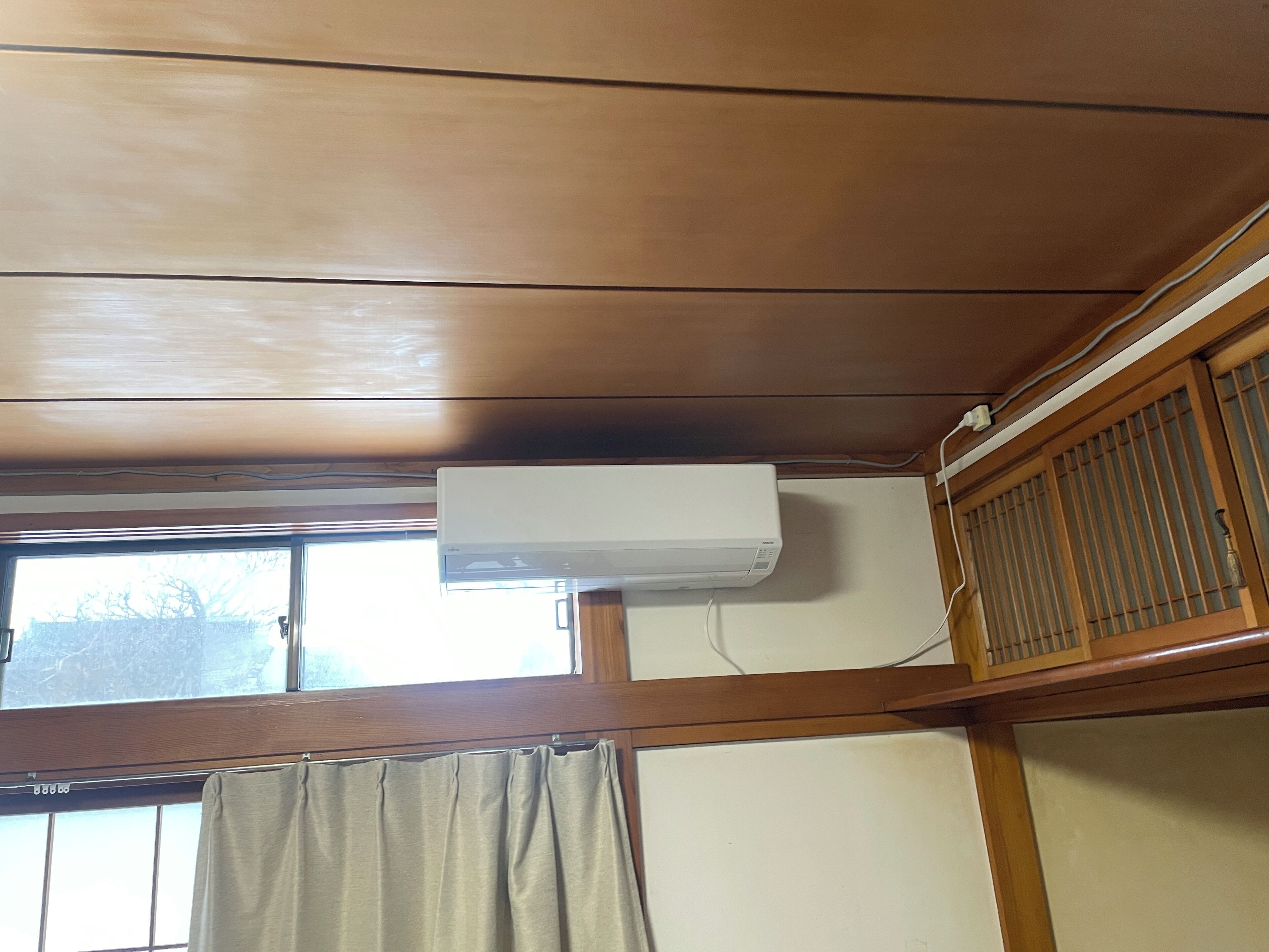 Ein Zimmer mit Holzwänden, einem fenster mit Vorhängen und einer Wand-Klimaanlage.