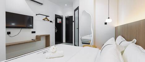 Una habitación de hotel moderna con una cama grande, un televisor de pantalla plana montado en la pared, una mesita de noche de madera y un espejo.