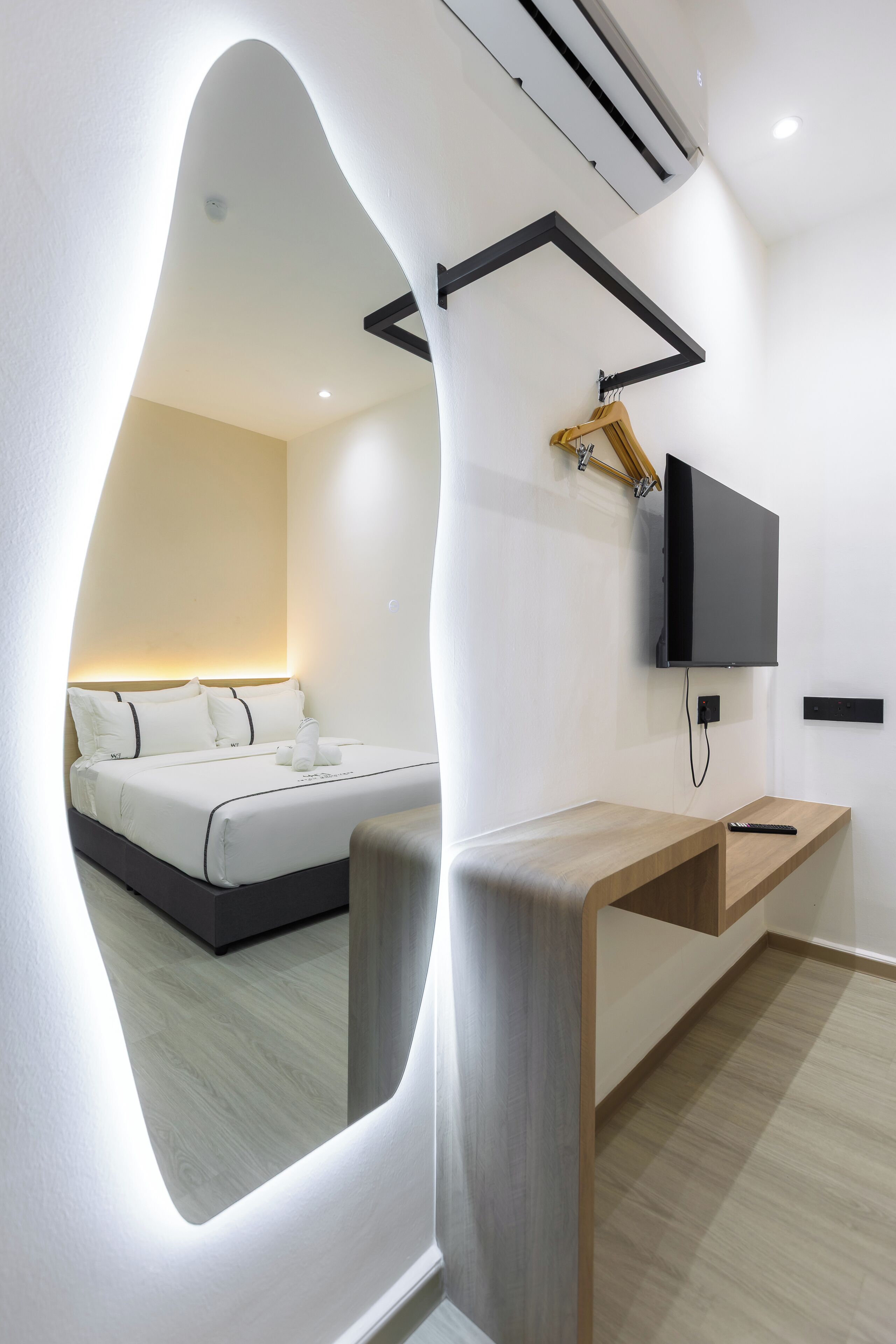 Una camera d'albergo moderna con un letto, una TV a parete e un tavolino consolle in legno.