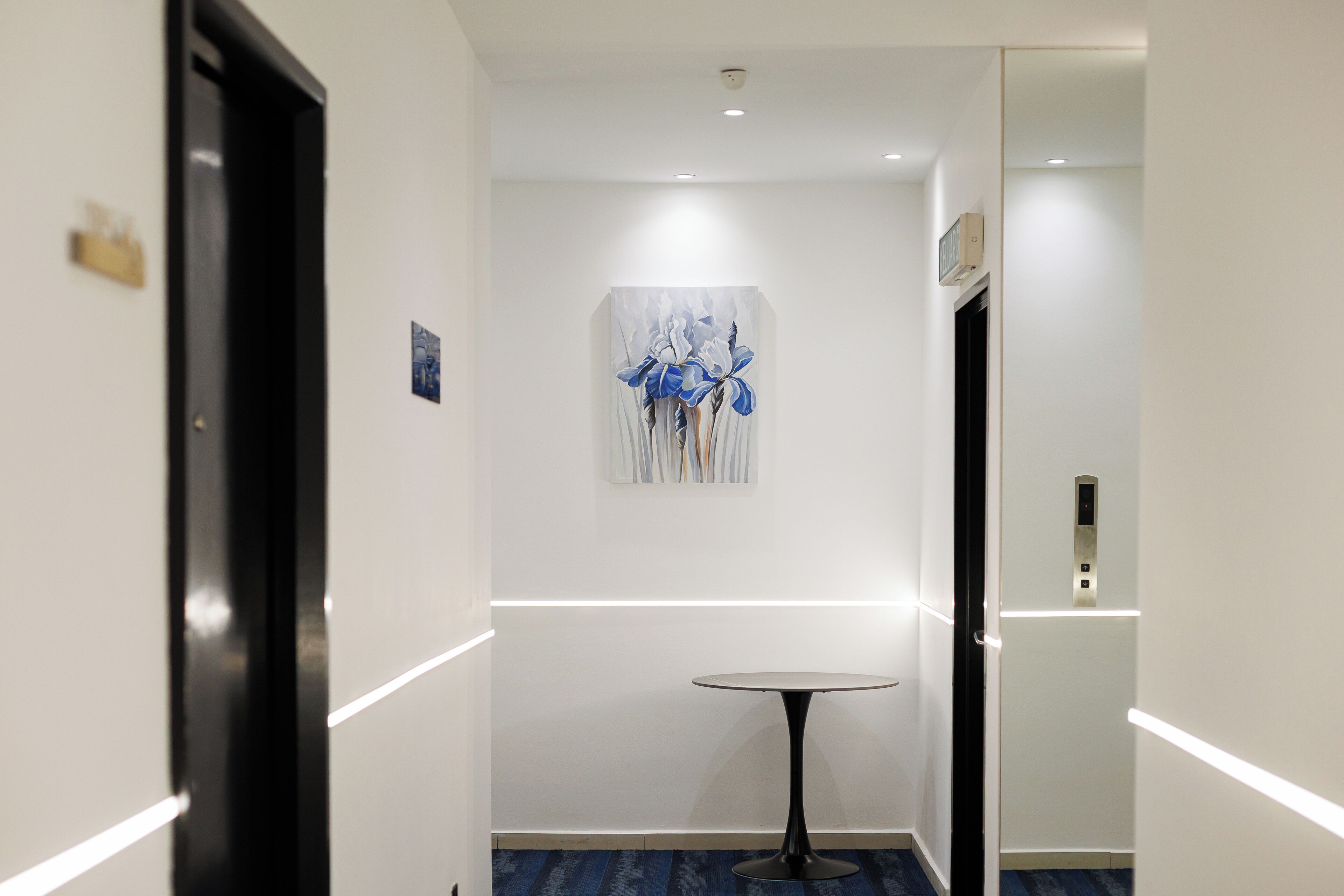 A hallway with a round table, a painting on the wall, and a door with a nameplate.