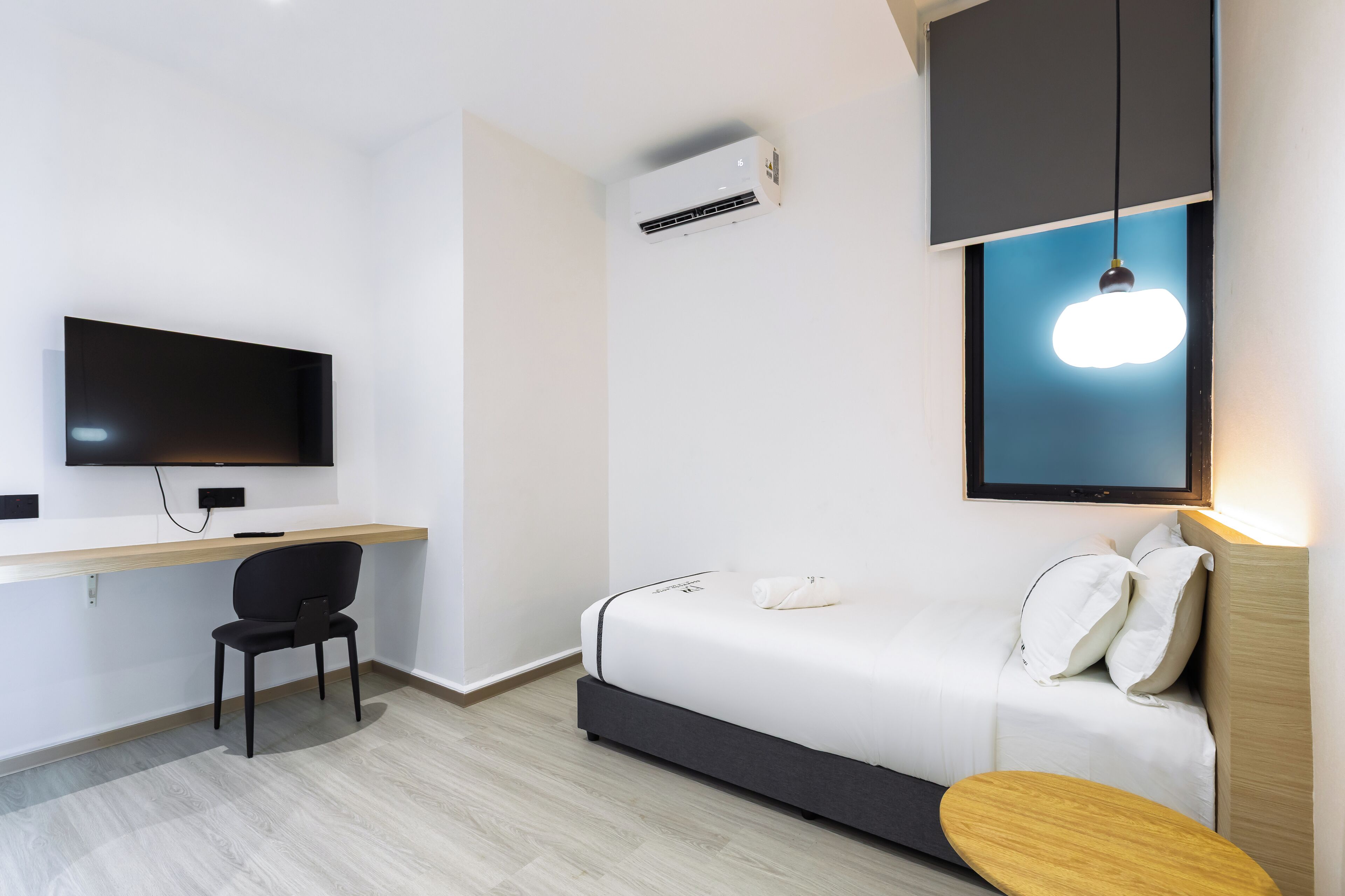 A modern hotel room with a bed, a desk, a chair, a TV, and an air conditioning unit.
